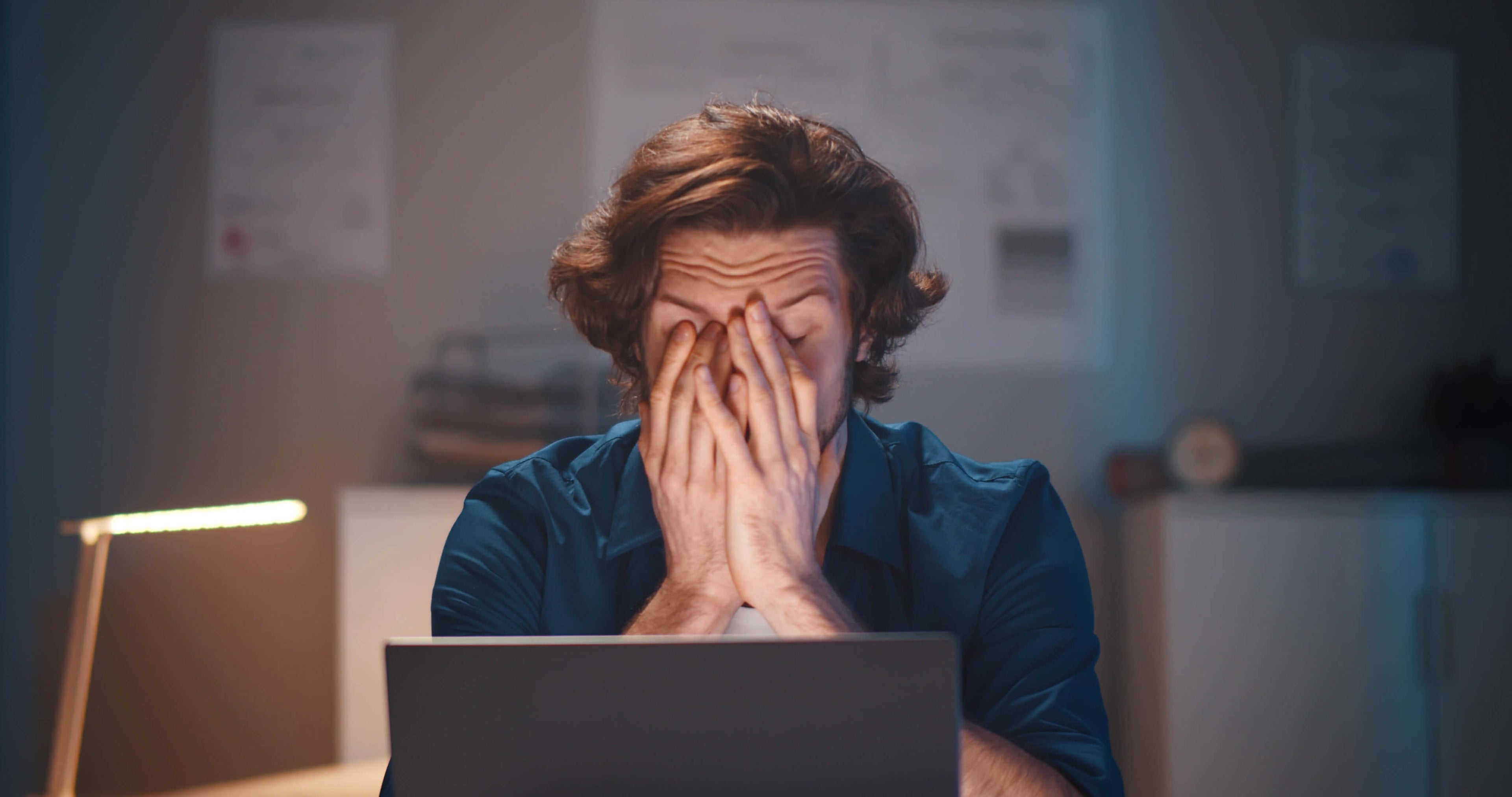 Man sitting at laptop late at night overwhelmed by blue light exposure from screen