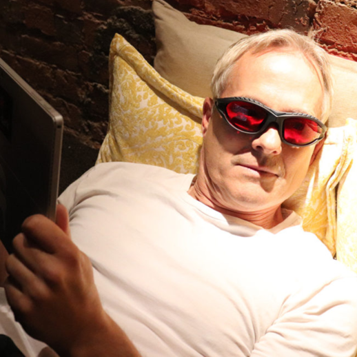 Man laying in bed wearing TrueDark Twilight Classic glasses while reading
