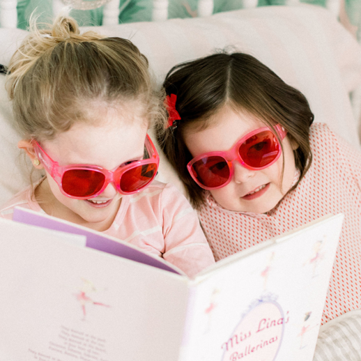 Girls wearing TrueDark Kids Pink Frame Twilights while reading a book