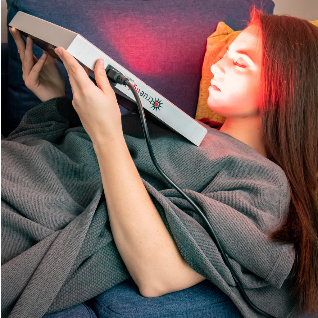 Woman covered with the TrueLight TrueLight Luna Red IR+FIR Blanket using the TrueLight Energy Square Light Therapy Device