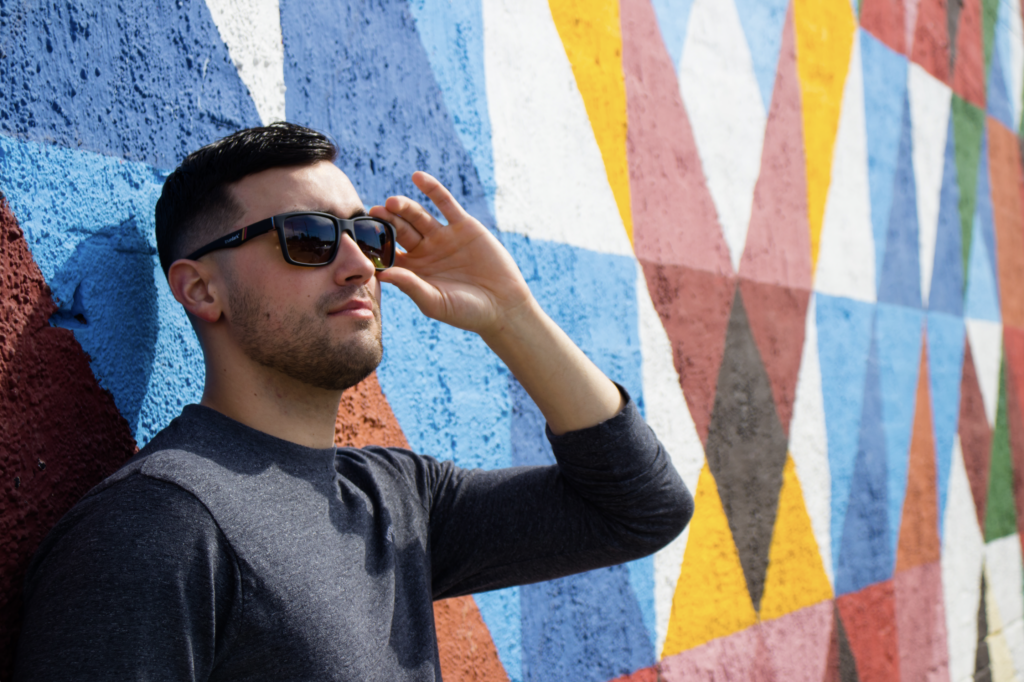 Man leaning against graffiti-ed wall wearing TrueDark Daylight Transition Fairlane Sunglasses