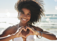 Portrait of a beautiful young woman making a heart shaped gesture with her hands at the beach