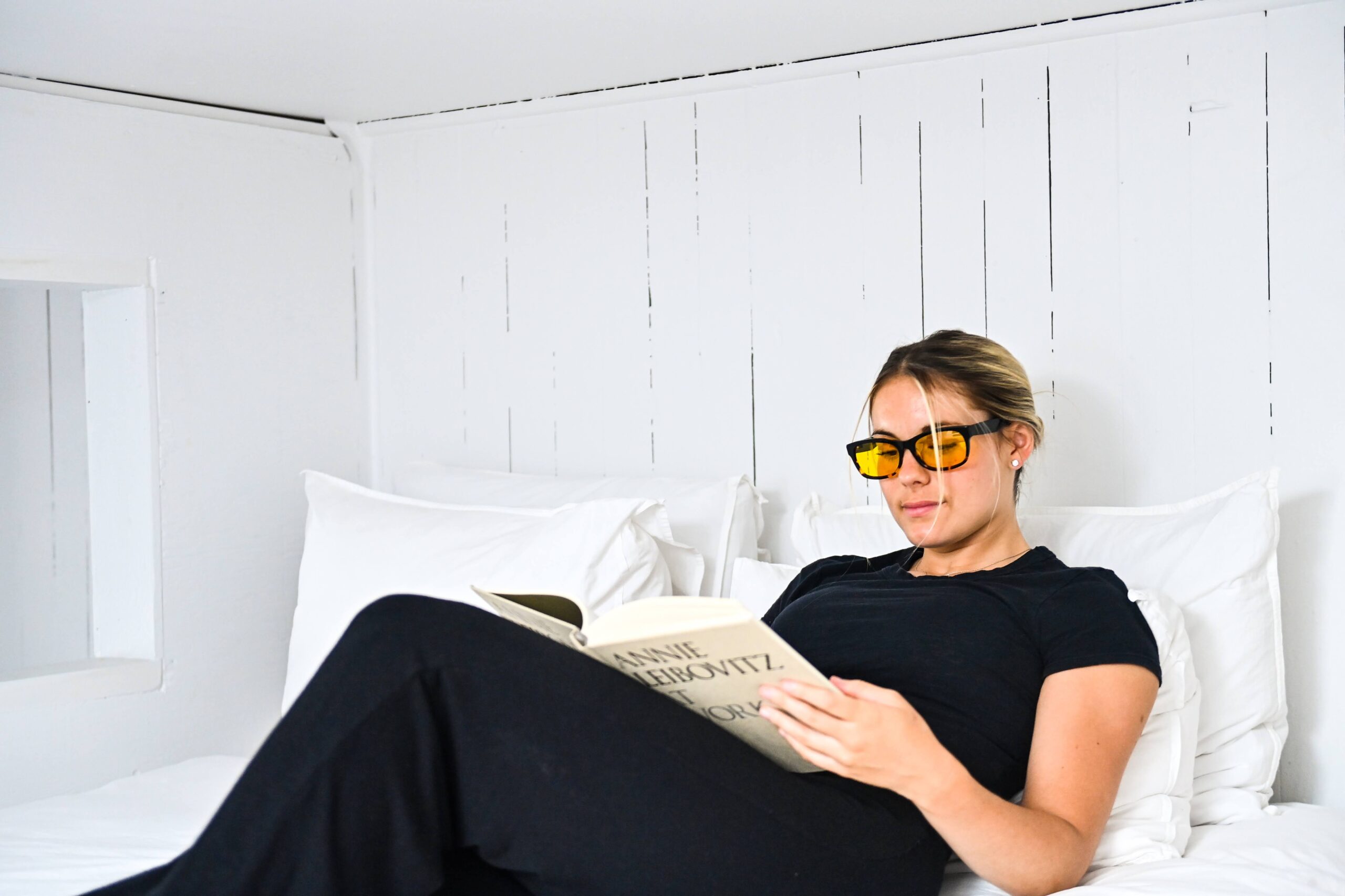 Woman relaxing on bed reading a book and wearing Amber TrueDark glasses